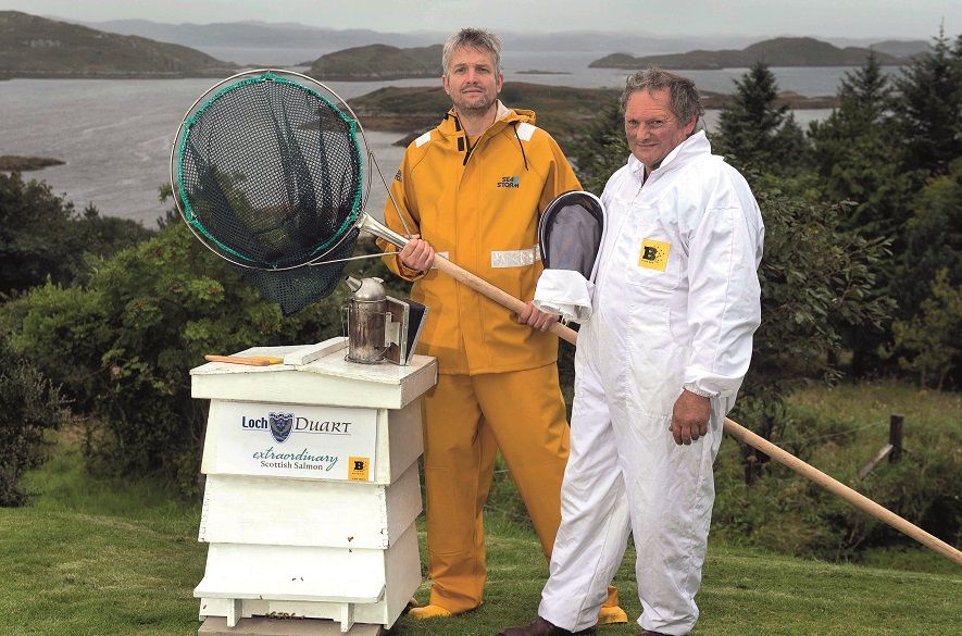 Two men next to a beehive one in Oilskins and one with a bee net