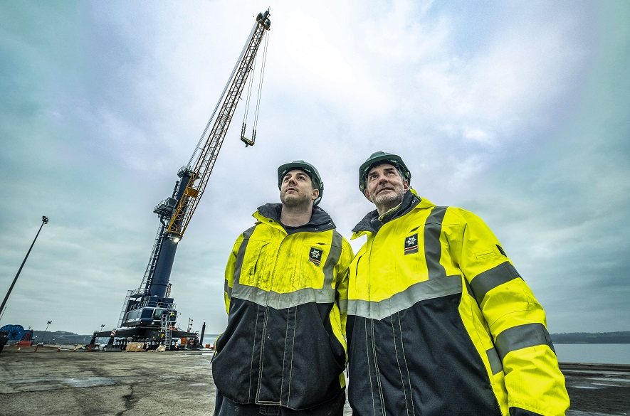 Two men in safety gear standing next to a crane